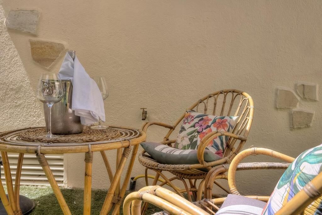 Una silla de mimbre con un cojín floral y una pequeña mesa redonda con una jarrón metálico y un mantel blanco.