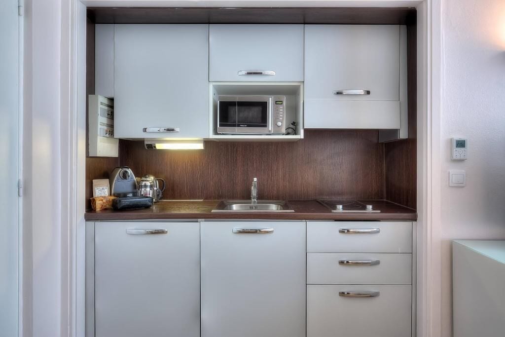 Een kleine keuken met witte kasten, een magnetron, een spoelbak en een koffiezetapparaat.