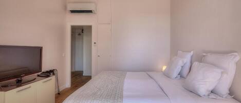 Un dormitorio con una cama, un televisor sobre un mueble y un equipo de aire acondicionado en la pared.