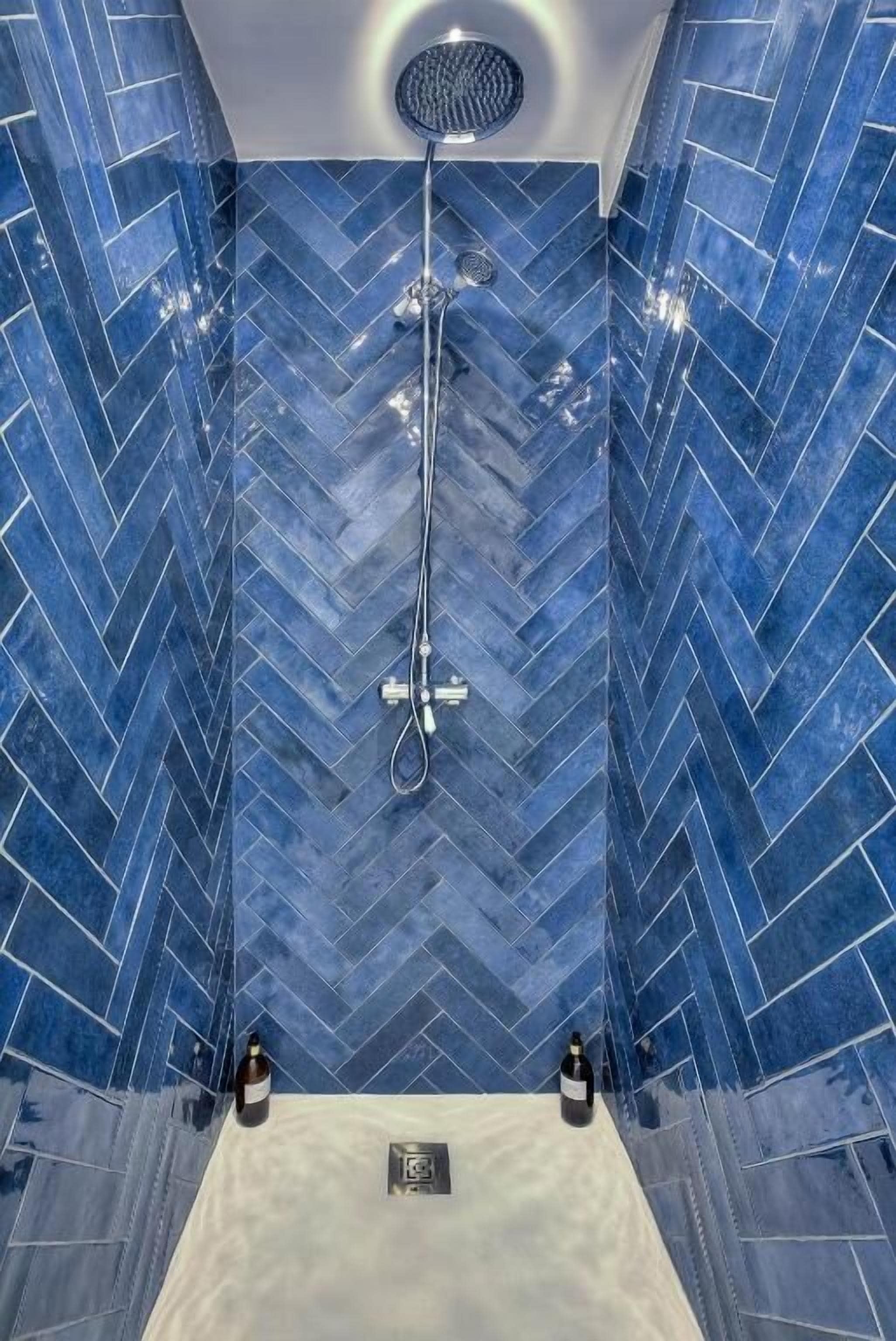 A shower with blue herringbone tiles and a handheld showerhead.