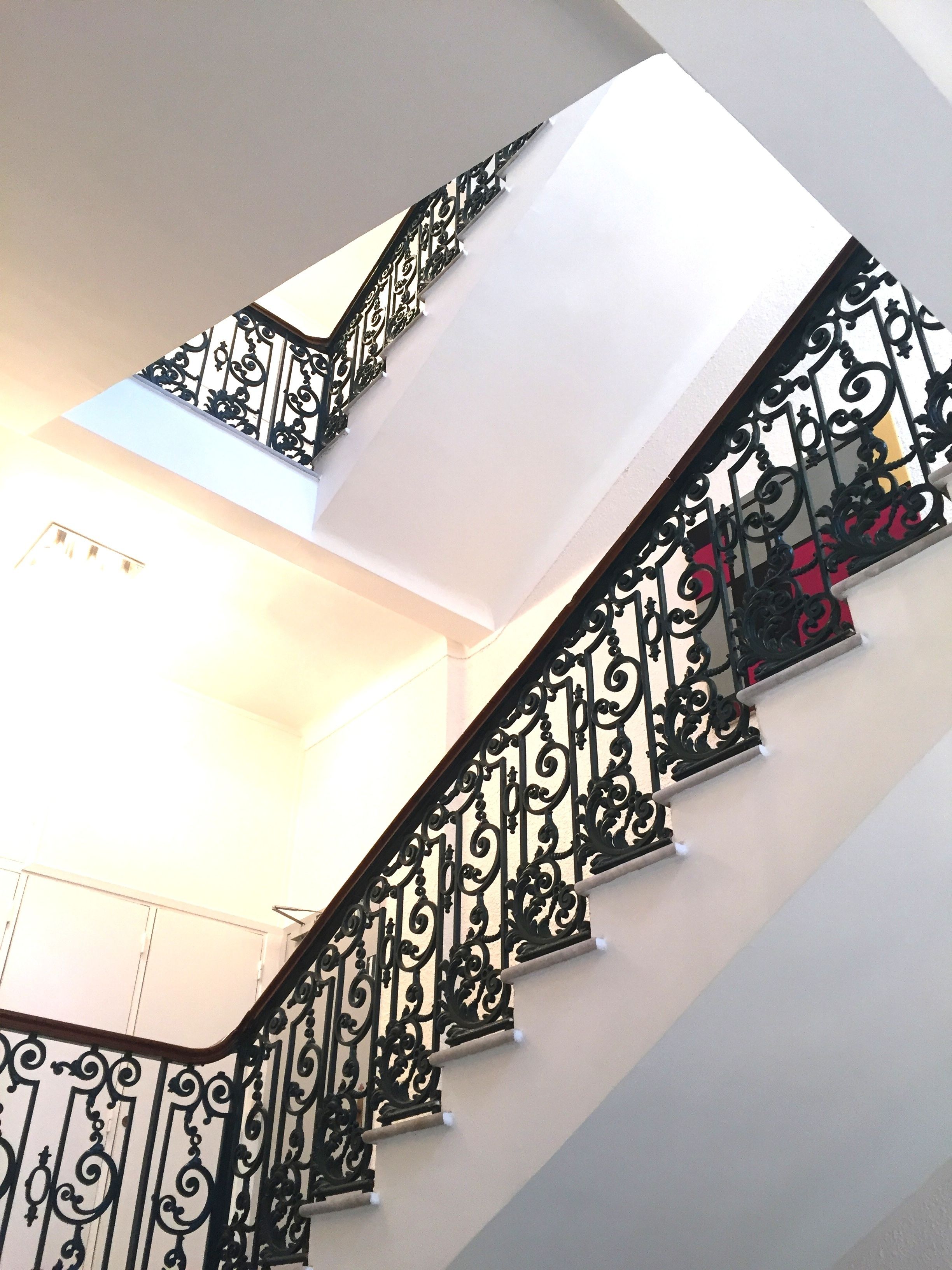 Eine Treppe mit aufwendiger schwarzer Metallgeländerung und einer weißen Wand.