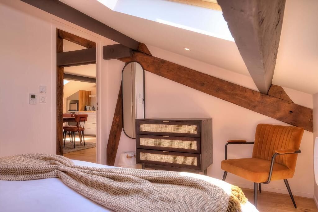 A bedroom with a sloped ceiling, a bed, a chair, and a bedside table.