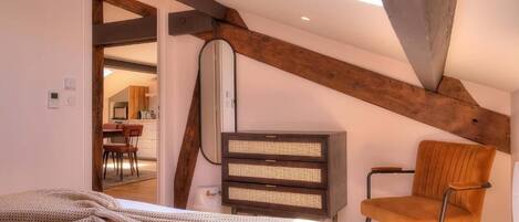 A bedroom with a sloped ceiling, a bed, a chair, and a bedside table.