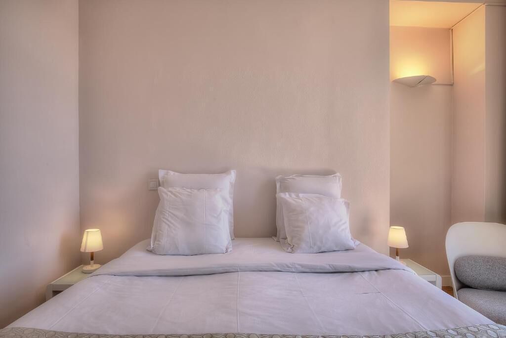 Un lit bien fait, avec du linge de lit blanc et des oreillers, deux lampes de chevet et une chaise avec un coussin.