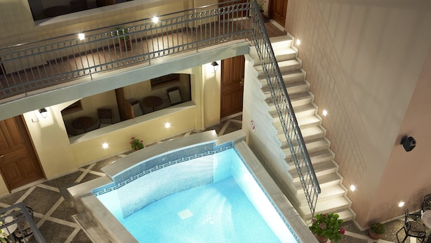 A multi-level hotel with a central swimming pool, outdoor seating, and a staircase connecting the floors. - Palazzo Vecchio Exclusive Residence (Rethymno)