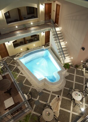A multi-level hotel with a central swimming pool, outdoor seating, and a staircase connecting the floors. - Palazzo Vecchio Exclusive Residence (Rethymno)
