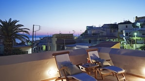 A rooftop terrace with two wooden lounge chairs and a table, overlooking a cityscape at dusk. - Palazzo Vecchio Exclusive Residence (Rethymno)