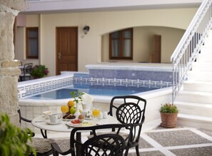 A dining table with breakfast items, a pool with a geometric tile pattern, and a staircase leading to an upper level.