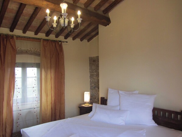 A bedroom with a wooden ceiling, a bed with white bedding, a nightstand with a lamp, and a window with curtains.