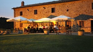 An outdoor dining area with stone walls and multiple tables and chairs under umbrellas. - Tenuta di Seripa (Sassetta)