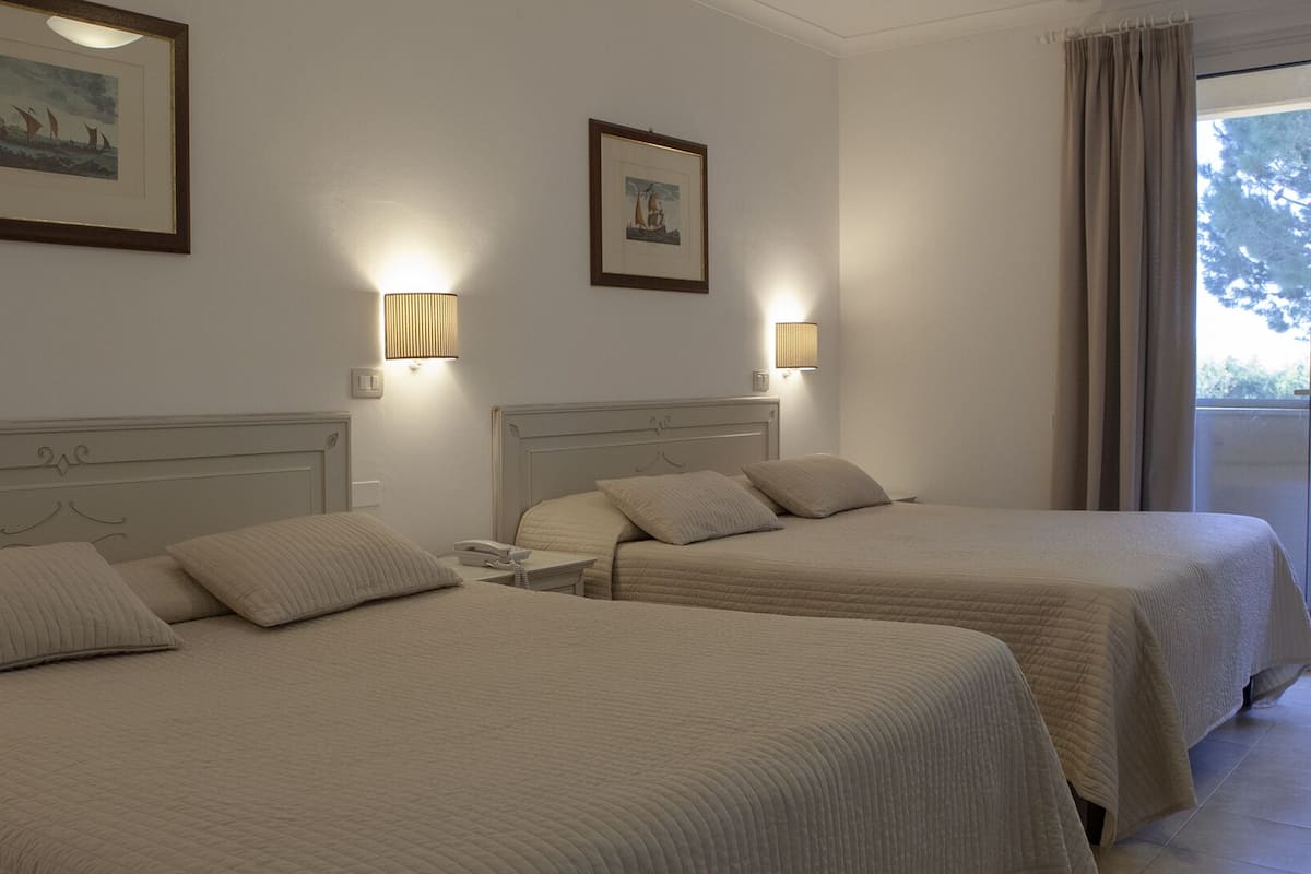Habitación de hotel con dos camas, cada una con cabecero, mesitas de noche y lámparas. Hay cuadros enmarcados en las paredes.