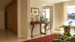 Un couloir avec une porte en bois, une console sur laquelle sont posés un vase et un tableau encadré, et un tapis rouge.