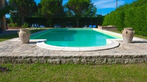 Une piscine rectangulaire bordée de pierres, entourée d’une pelouse verdoyante et d’arbres.