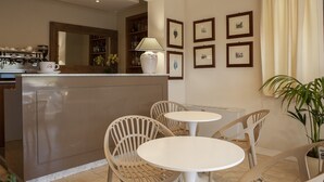 Une cuisine moderne équipée d’une machine à café, d’un réfrigérateur et d’un coin repas avec deux tables rondes et des chaises en osier.