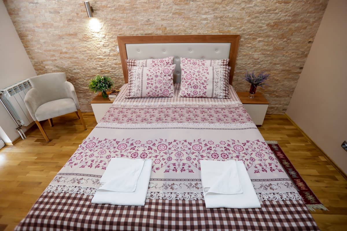 A neatly made bed with floral bedding, a wooden headboard, and a checkered bed runner.