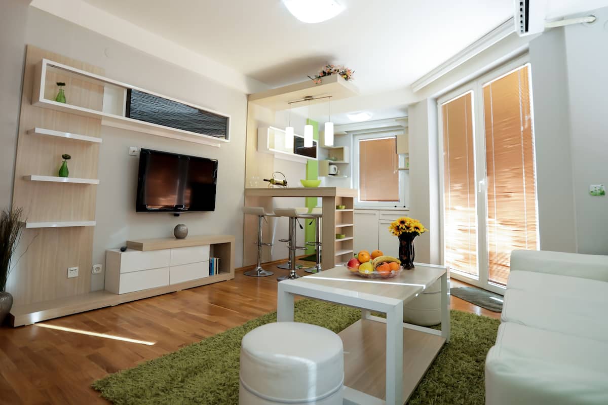 A modern living room with a flat-screen TV, a white sofa, a coffee table with fruit, and a green rug.