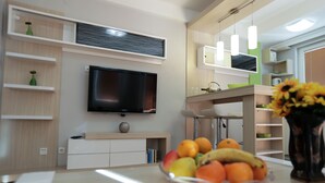 Una sala de estar moderna con un televisor de pantalla plana, estanterías empotradas, un comedor y un frutero sobre la mesa.
