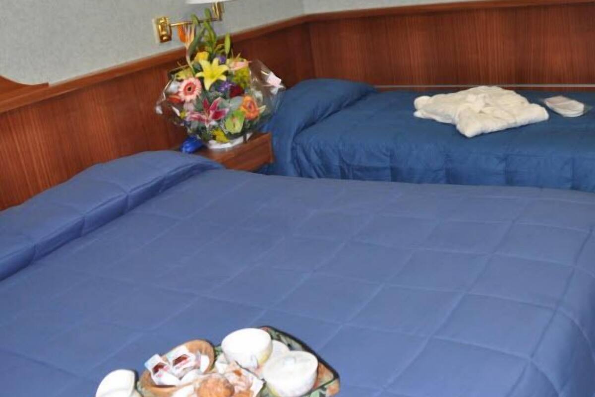 A hotel room with two beds, a floral arrangement, and a painting on the wall.