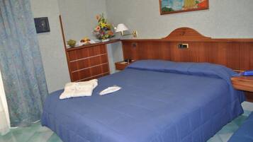 Une chambre d’hôtel avec un grand lit, une tête de lit en bois, une table de chevet avec une lampe, une petite table sur laquelle est posé un vase de fleurs, et un tableau au mur.