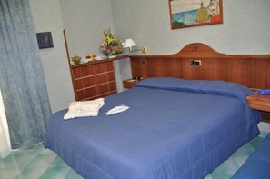A hotel room with a large bed, a wooden headboard, a nightstand with a lamp, a small table with a vase of flowers, and a painting on the wall. - Hotel Fiorenza (Salerno)