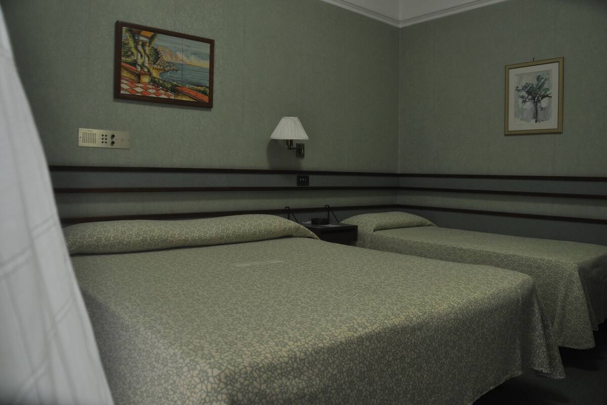 A hotel room with two beds, a nightstand, a lamp, and two framed pictures on the walls.