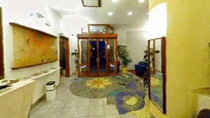 Un vestíbulo con mostrador de recepción, puerta de cristal de entrada, alfombra estampada y planta en maceta.