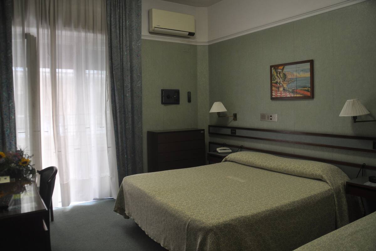 A hotel room with two beds, a desk with a chair, a lamp, and a painting on the wall.