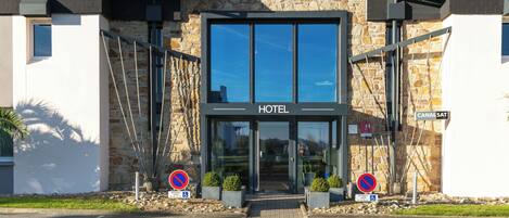 Entrada de un hotel con fachada de piedra, puerta de cristal y un cartel que dice 'BRITHOTEL'.