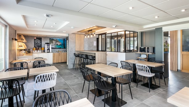 Un restaurante moderno con varias mesas y sillas, una zona de cocina y una barra con la carta.