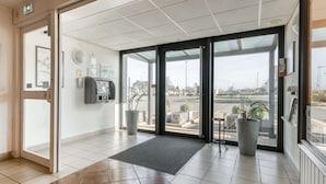 Un moderno vestíbulo de hotel con entrada de puerta de cristal, una recepción, un cajero automático y plantas en macetas.