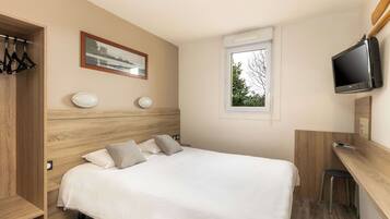 A bedroom with a bed, a desk, a television, and a window.