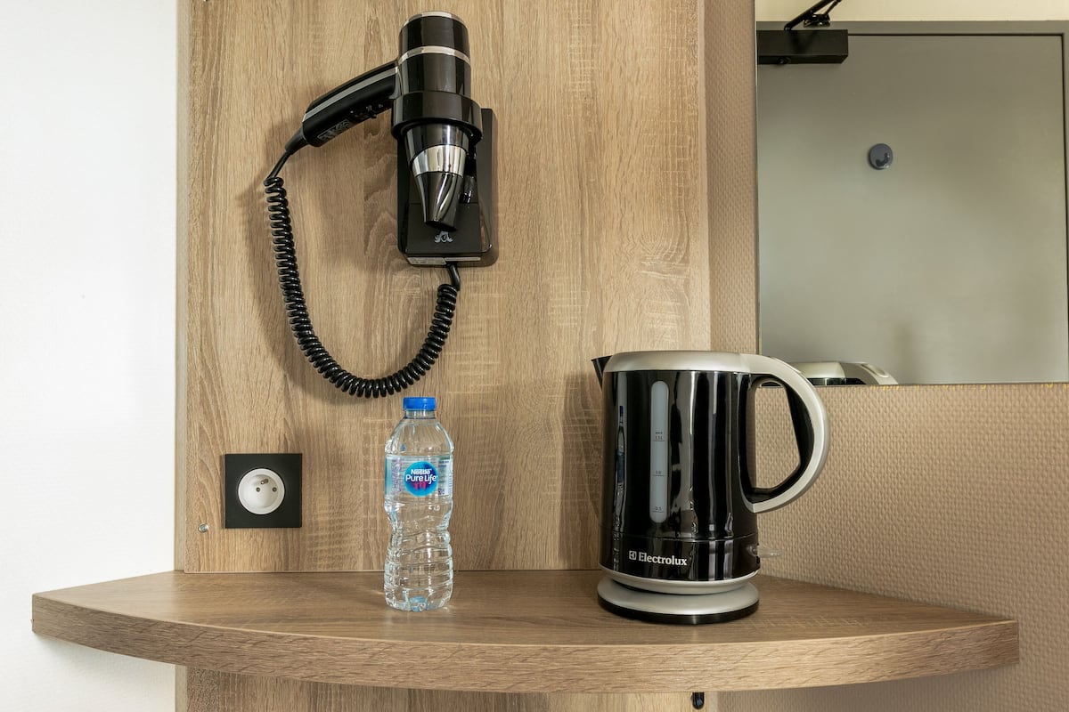 Een houten plank met een haardroger, een waterfles en een zwarte koffiezetapparaat.