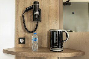 A wooden shelf with a hair dryer, a water bottle, and a black coffee maker. - Brit Hotel Iroise (Plougastel-Daoulas)
