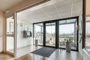 Een hotel receptie met een glazen deur, een receptiebalie, een telefoon, een plant en uitzicht op het buiten.