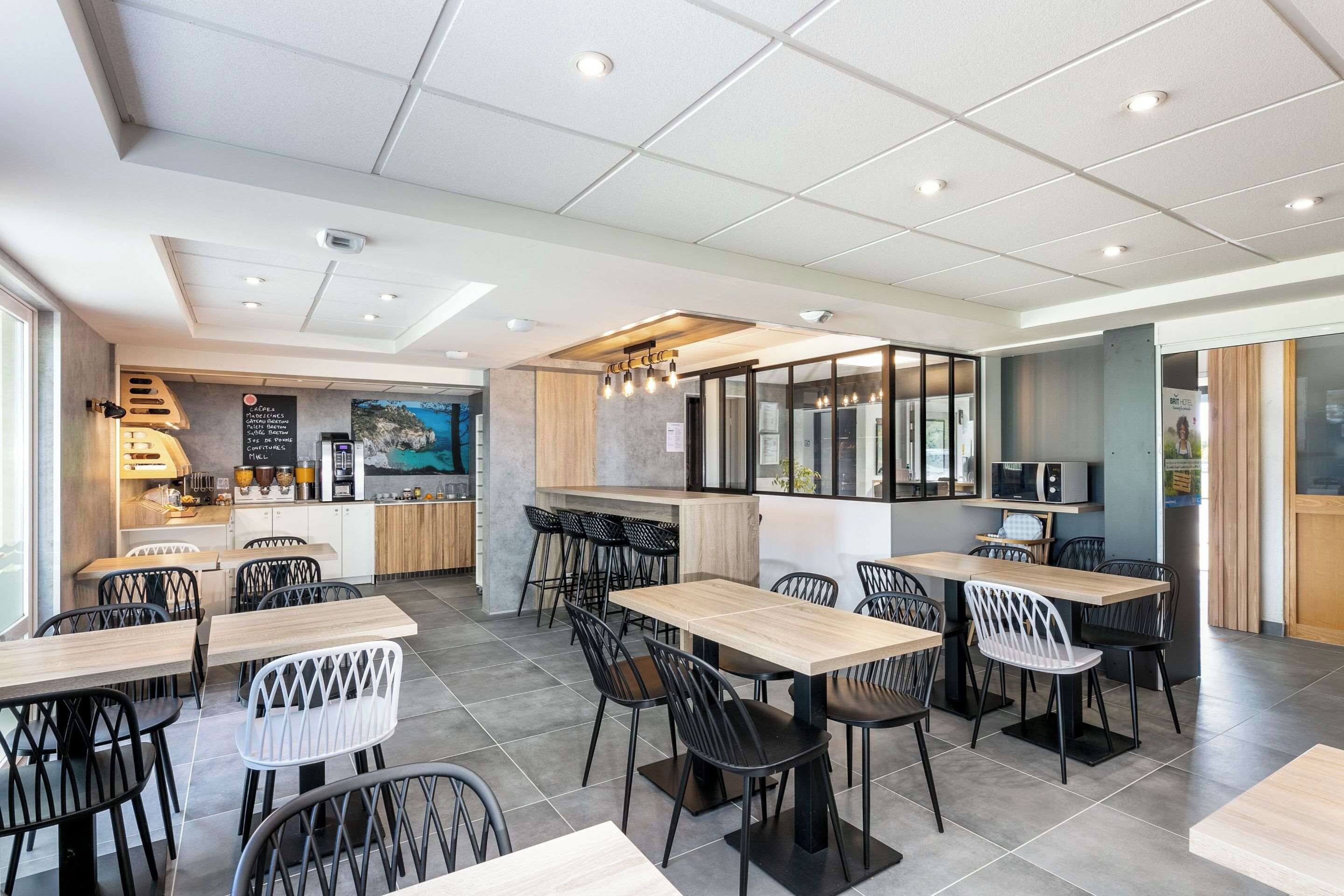Un comedor moderno con varias mesas y sillas, una encimera de cocina y vistas al mar a través de grandes ventanales.