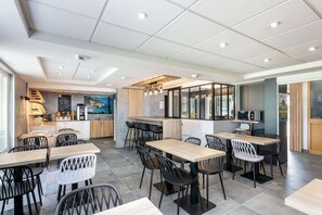 Un comedor moderno con varias mesas y sillas, una encimera de cocina y vistas al mar a través de grandes ventanales.