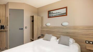 A hotel room with a bed, a wooden headboard, a nightstand, a bedside table, a coffee maker, a wardrobe, and a framed picture on the wall.