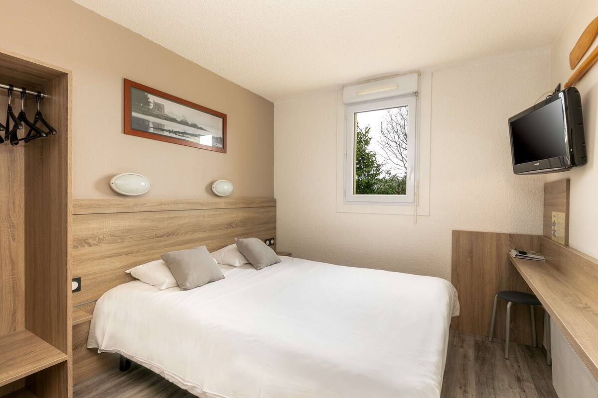 Een slaapkamer met een bed, een bureau, een televisie en een raam.