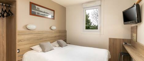 Un dormitorio con cama, escritorio, televisor y ventana.