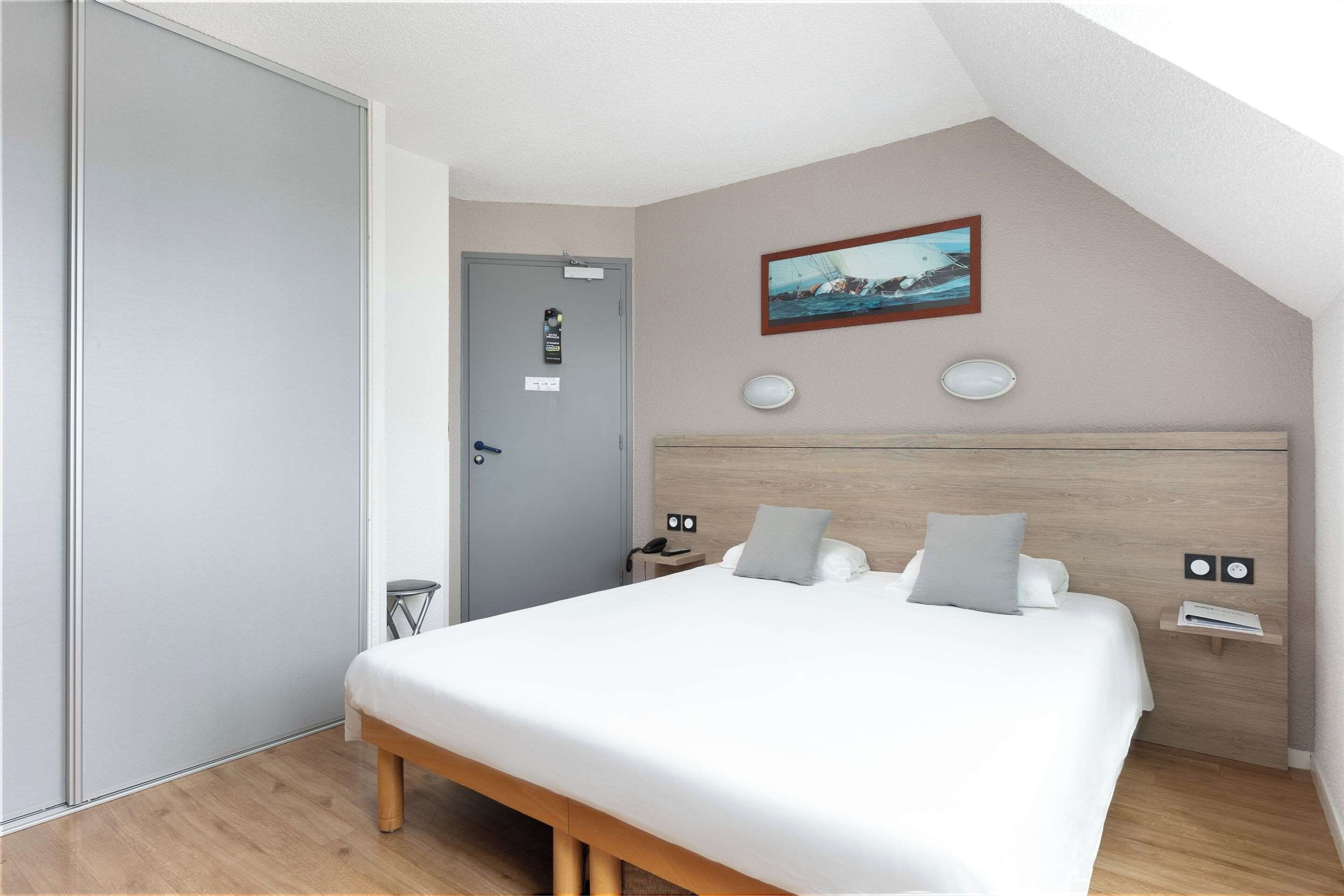 A bedroom with a bed, bedside tables, a headboard, a painting, and a door.