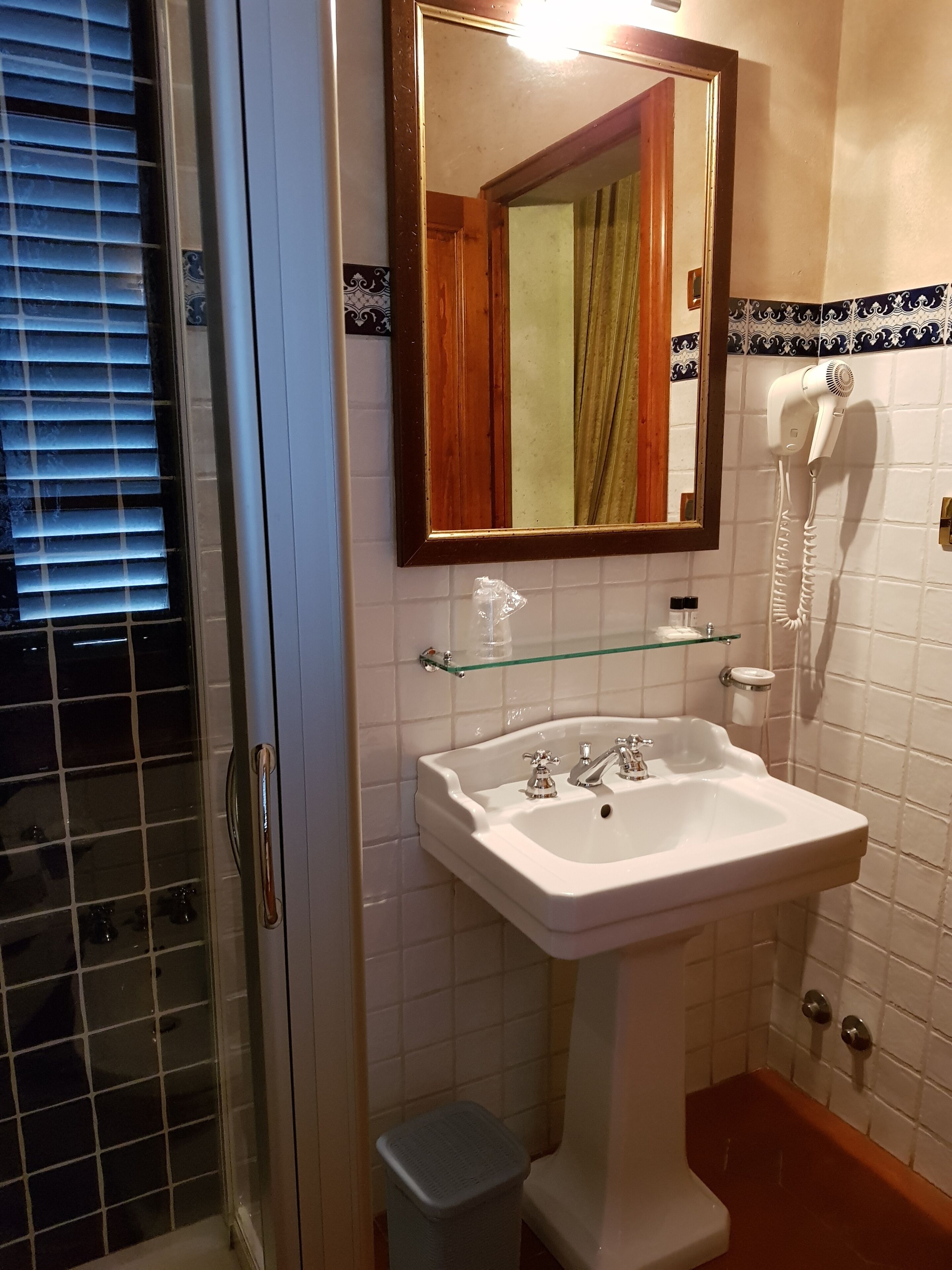 A bathroom with a white sink, a glass shelf, a mirror, and a hairdryer.