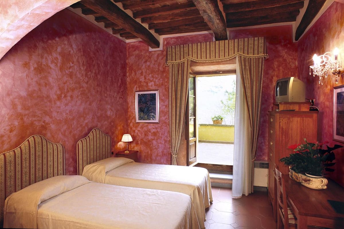 A room with two beds, a television, a lamp, and a window with curtains.