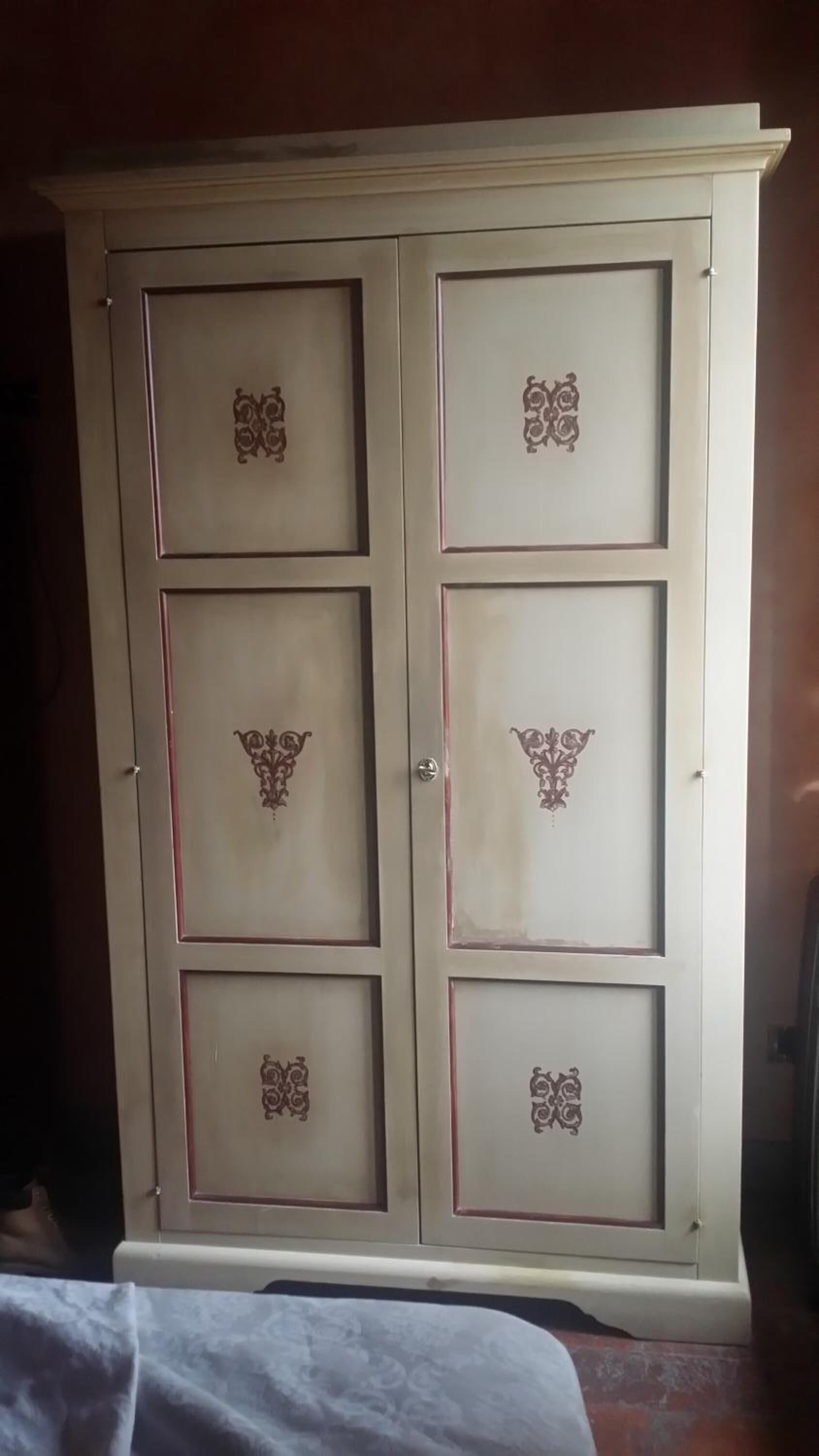 Un armario grande de color crema con patrones decorativos en las puertas y cajones.