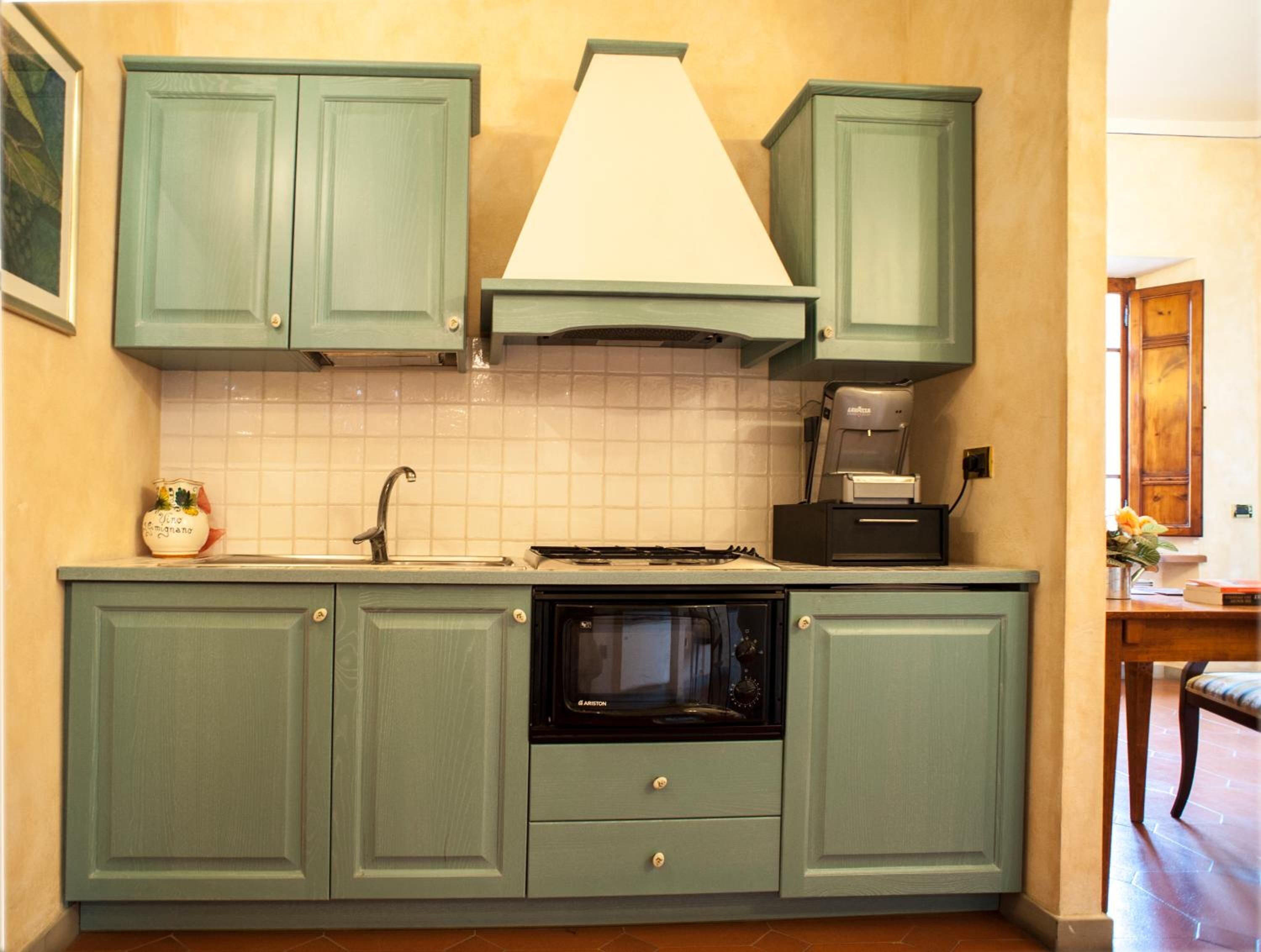 A kitchen with green cabinets, a white tiled backsplash, a stove, and a coffee maker.