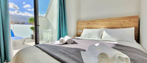 A hotel room with a large bed, a wooden headboard, and a view of the sky through a sliding glass door.