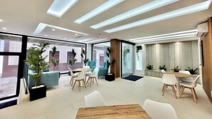 A modern hotel lobby with a wooden table, white chairs, and potted plants. - Puerto Azul (Puerto de la Cruz)