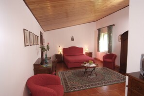 Una habitación acogedora con techo de madera, un sofá rojo, un sillón rojo, una mesita con un florero y una cama con una colcha roja.
