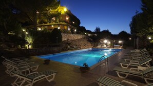 Ein Pool mit Liegestühlen, eine Steinsäule und ein Gebäude mit Lichtern im Hintergrund.