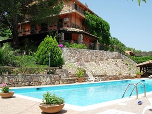 Una piscina con un muro de piedra y un edificio con balcones al fondo.