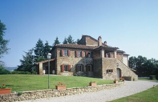 A stone house with a sloped roof, multiple windows, and a gravel driveway.